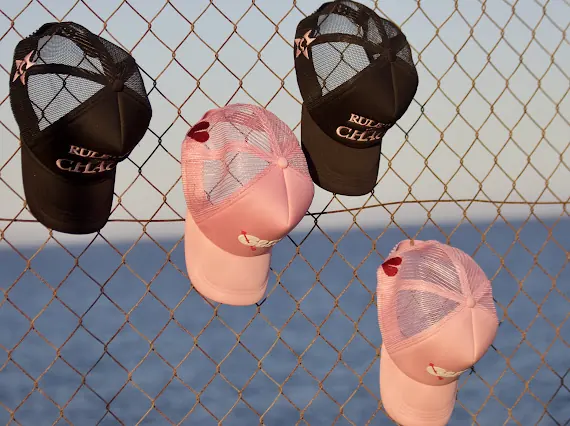 Pink and black GALNEZ caps hanging on a fence by the sea